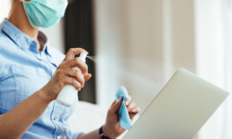 Woman cleaning laptop with disinfectant spray